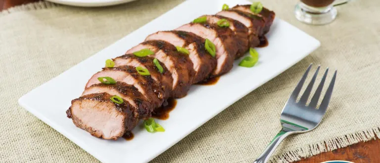 A glazed pork tenderloin on a plate with chives sprinkled on top.