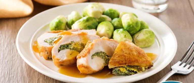 A stuffed chicken breast on a plate beside brussels sprouts.