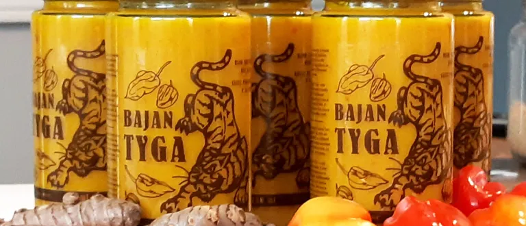 Jars of bright yellow hot sauce with the name Bajan Tyga; with ginger and scotch bonnet peppers