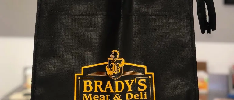 Insulated shopping bag with the Brady's Meat & Deli logo printed on it sitting on a counter.