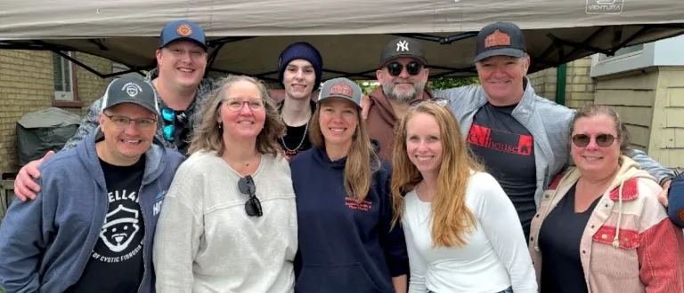 A group of 9 smiling people standing in front of a tent. Mike Farwell is on the lower-left; Rob Brady is in the upper-right.