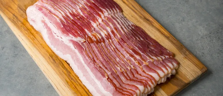 Sixteen slices of smoked pork side bacon on a wooden plank